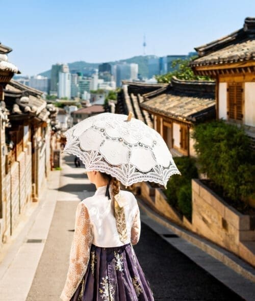 South Korea, Seoul. Woman in hanbok in Bukchon Hanok Village. Girl wearing traditional dress and costume. Korean tradition. City skyline in the background. Travel in summer or spring. Back view.